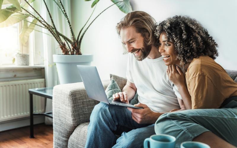 a man and a woman sitting on a couch looking at a laptop
